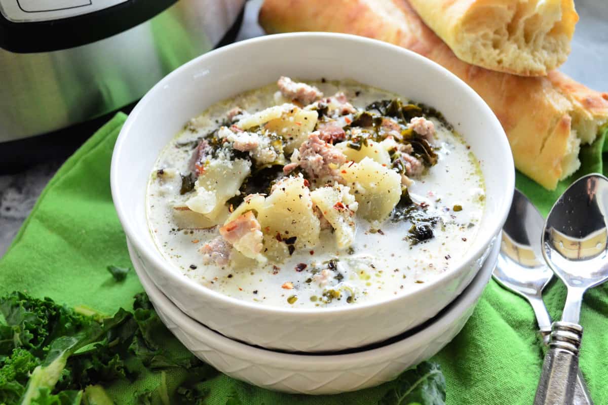 Two bowls stacked on green cloth with top bowl full of white soup with kale, potatoes, and bacon visible.