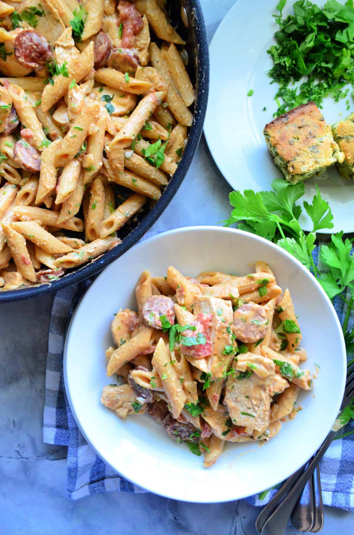 Top View Plated Penne pasta with white sauce, herbs, and meat next to pan full of remaining pasta.