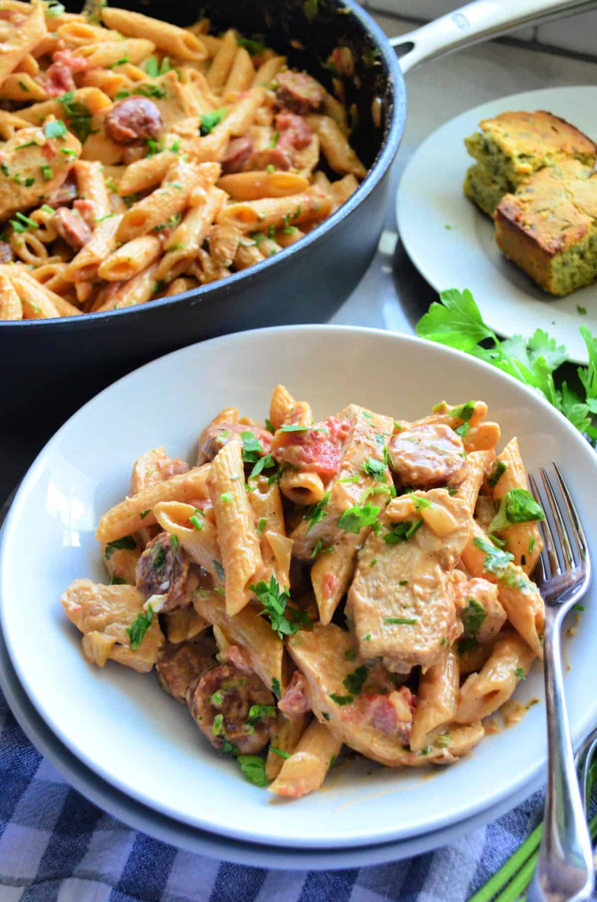 Top view of sliced sausage, penne, green herbs, chicken tossed in light sauce plated and in pan.