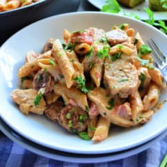 Plated Penne pasta with white sauce, herbs, meat and fork.