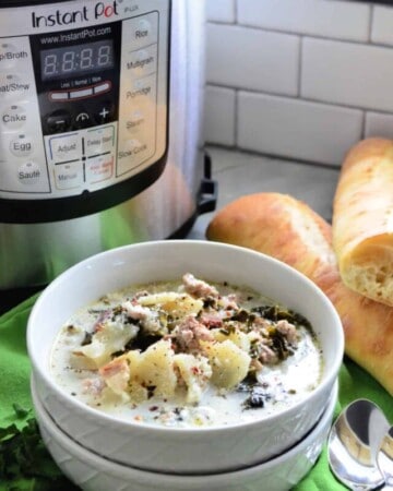 Bowl of creamy soup with potatoes and herbs on top in front of instant pot.