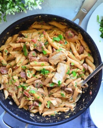 Top view of Pan full of sliced chicken, penne pasta, white sauce, sausage.