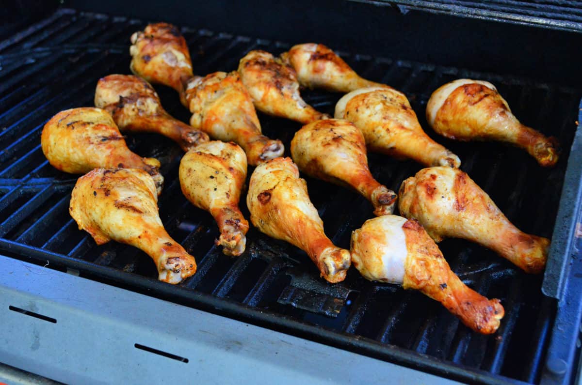 14 golden brown Chicken drumsticks cooking on the grill.