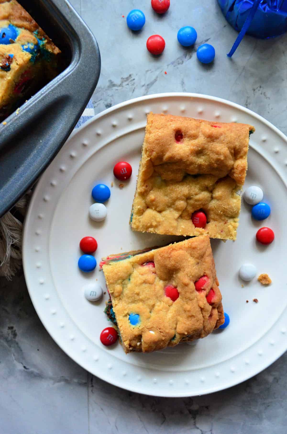 Top view of a white plate with two cookie bars and red, white, and blue M&M's on the plate.