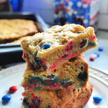 Stacked M&M Cookie Bars with red, white, and blue M&M's in the background.