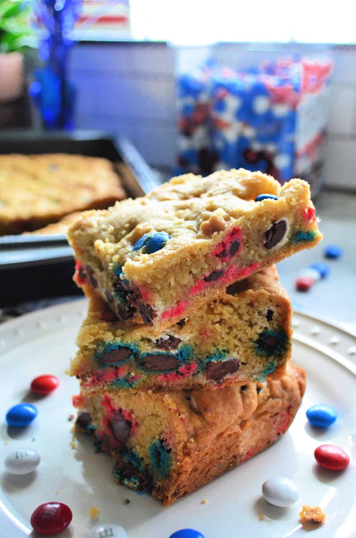 Stacked M&M Cookie Bars with red, white, and blue M&M's in the background.