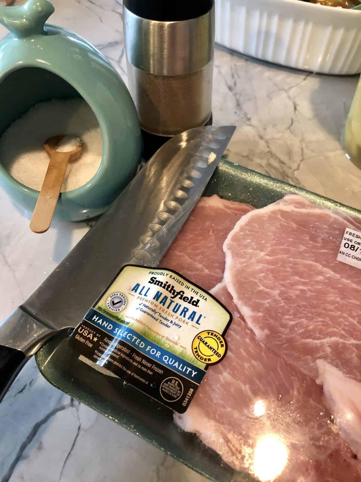 Smithfield All Natural pork chops uncooked and in package next to knife, salt, and pepper.