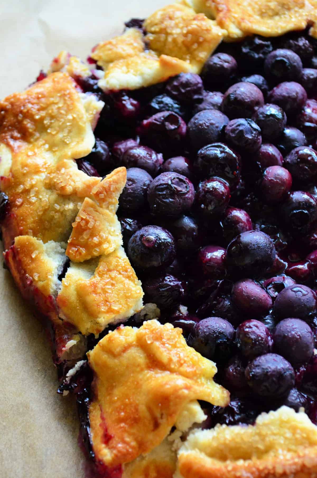 closeup partial view of flakey pie crust with cooked blueberry filling glistening.