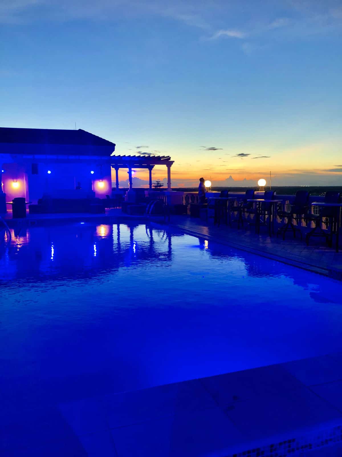 Blue filtered pool and pool house with patio seating during sunset.