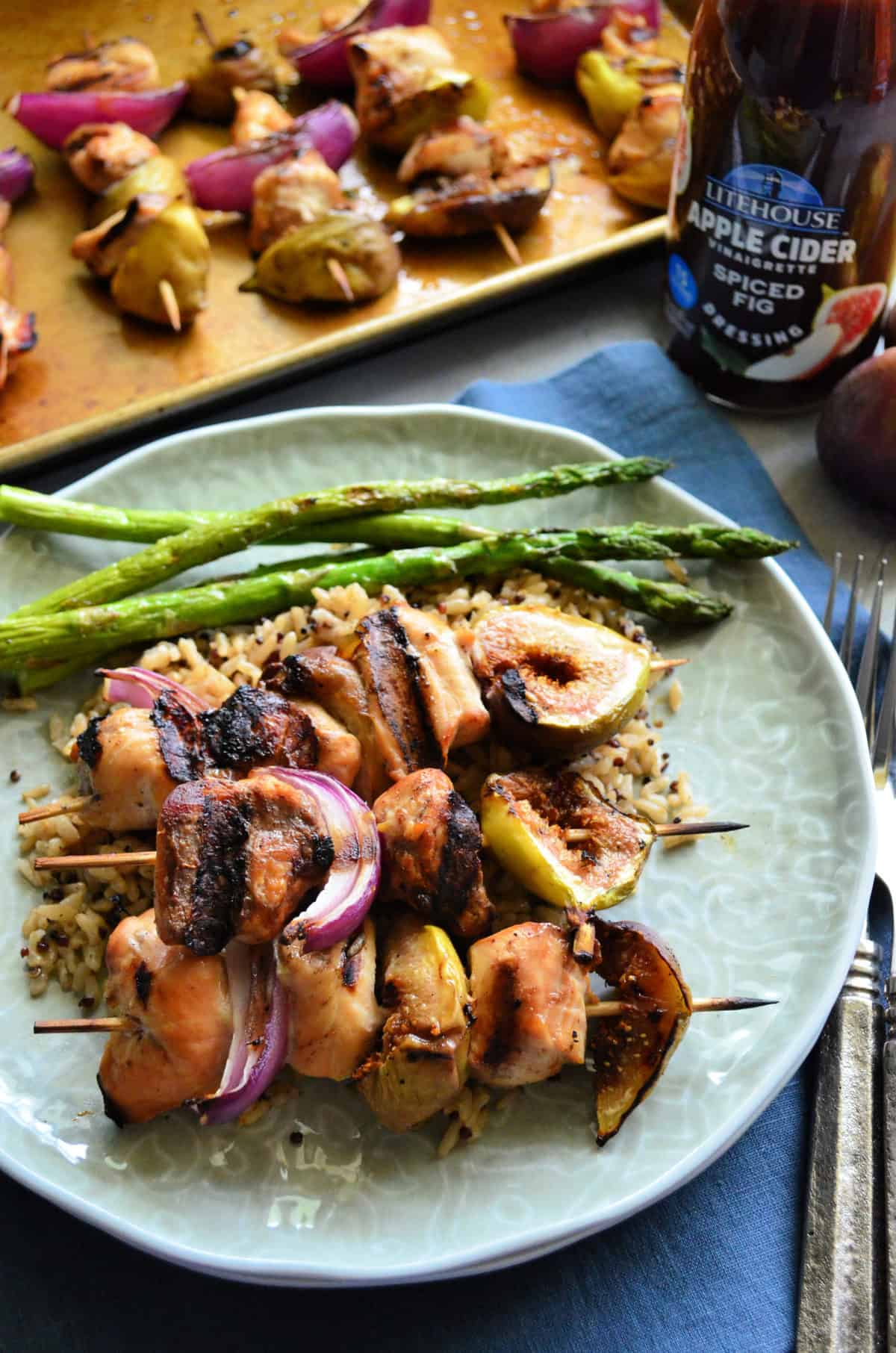 plated chicken skewers with onion, figs, rice, asparagus in front of dressing bottle.