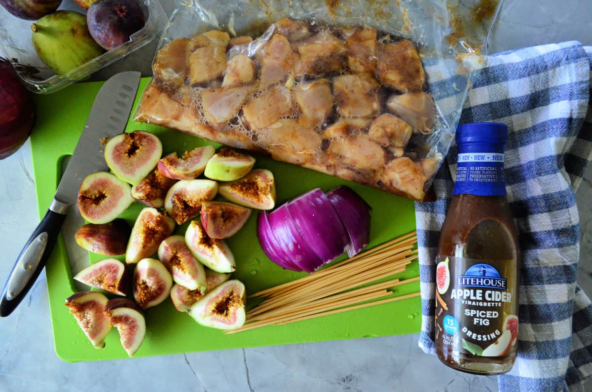 bag with marinading chicken, quartered fresh figs, sliced red onion, dressing, and pasta on cutting board.