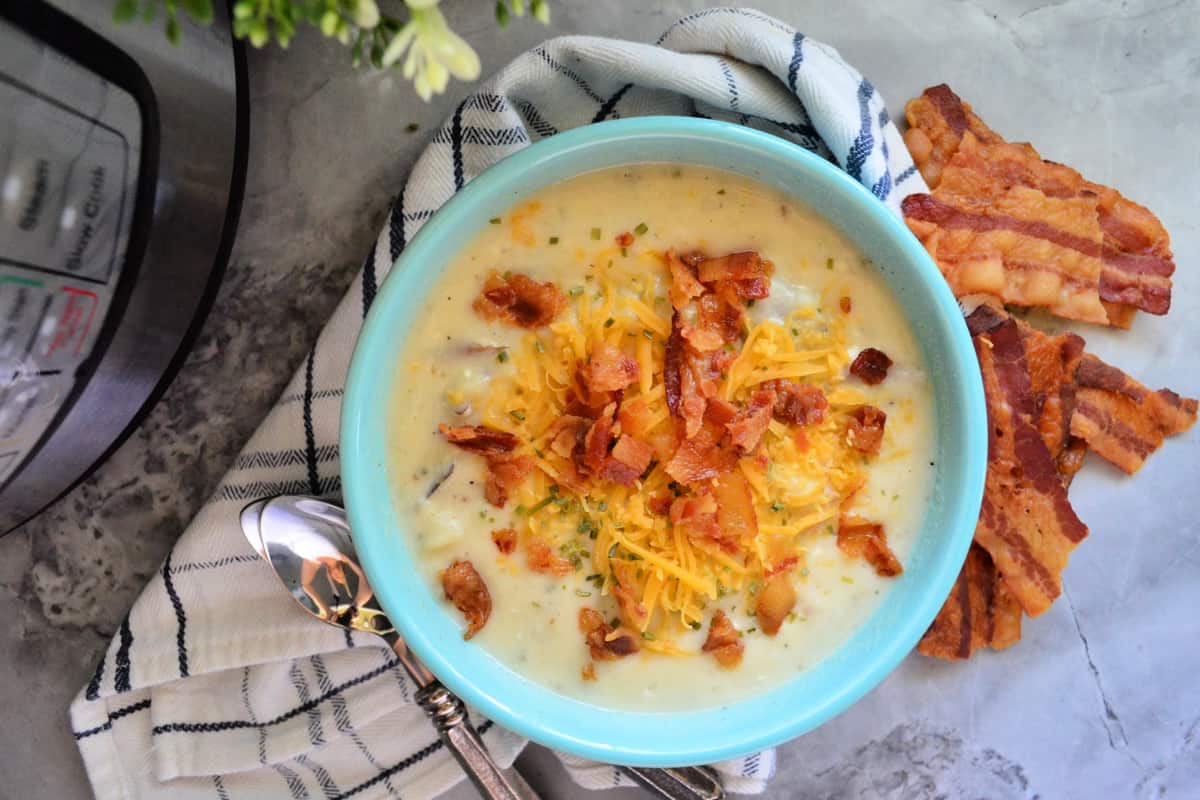 top view bowl of creamy soup topped with herbs, bacon, and cheddar on countertop with bacon.