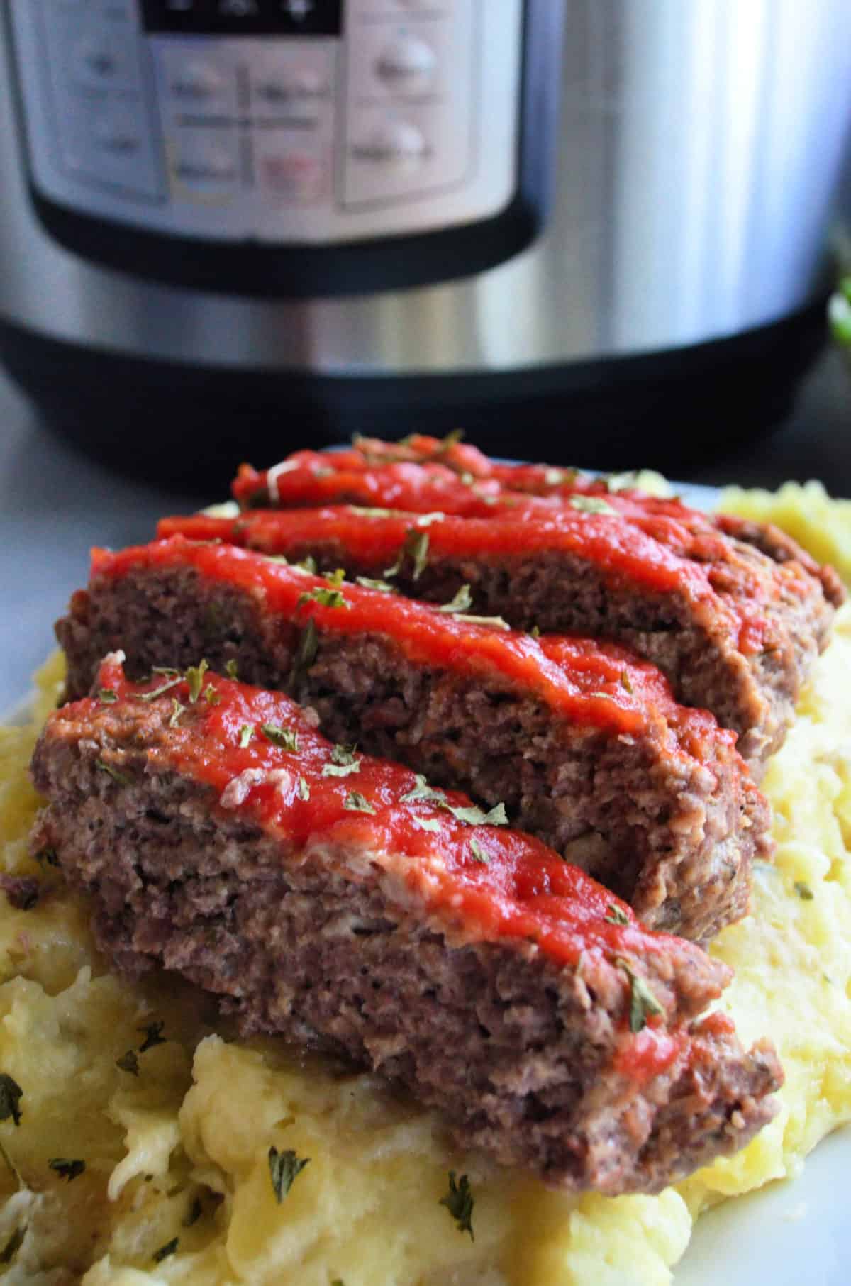 closeup front view of sliced meatloaf topped with herbs and red sauce over mashed potatoes.