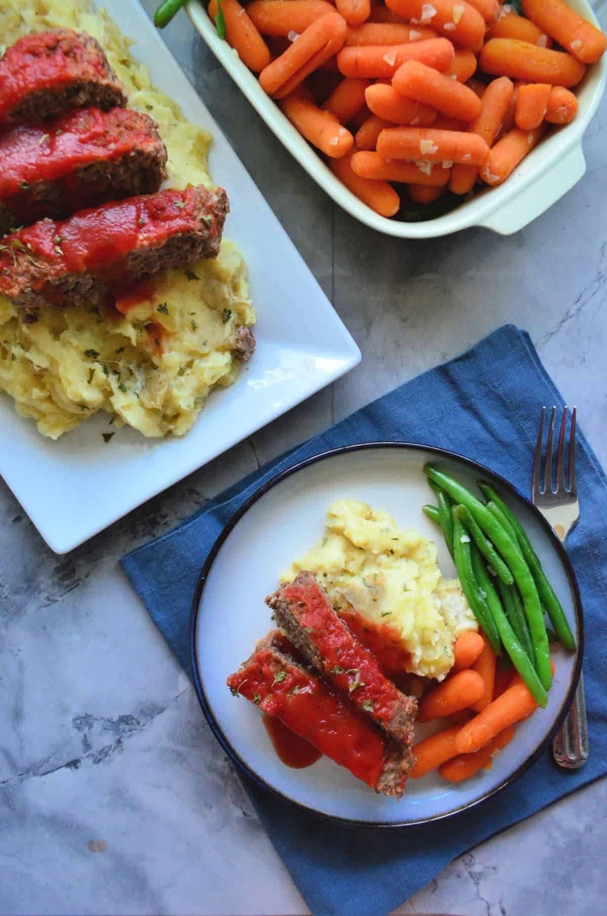 meatloaf platter next to dish of carrots by plate of both dishes with green beans.