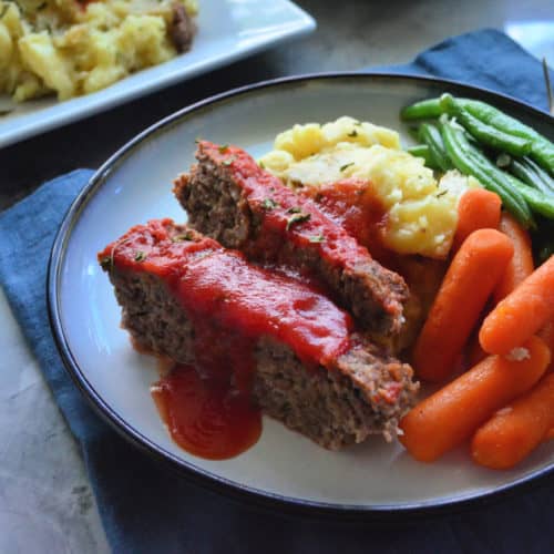 Plated Slices of meat loaf served with carrots, green beans, and mashed potatoes.