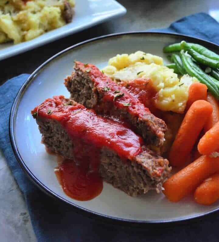 Plated Slices of meat loaf served with carrots, green beans, and mashed potatoes.