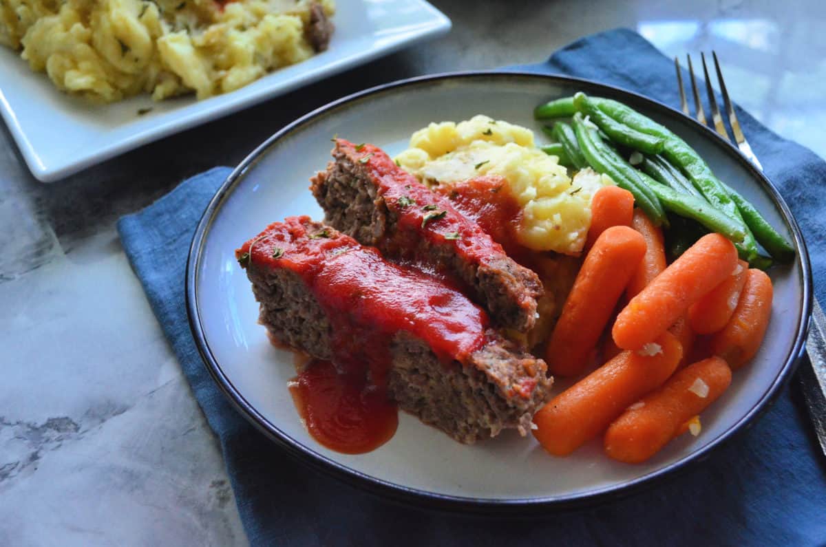 Plated Slices of meat loaf served with carrots, green beans, and mashed potatoes.