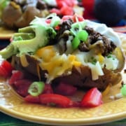 Side View Plated Baked potato loaded with sour cream, tomato, olives, avocado, and shredded cheese.