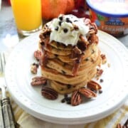 Plated Chocolate Chip pancakes stacked high, topped with pecans, chocolate chips, whipped cream, and caramel sauce.