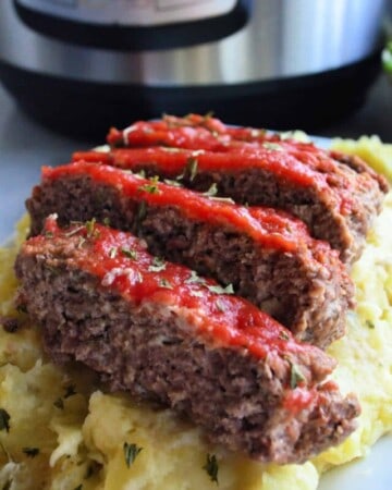 Platter of Golden herbed mashed potatoes topped with 5 slices of meatloaf dripping with red sauce.