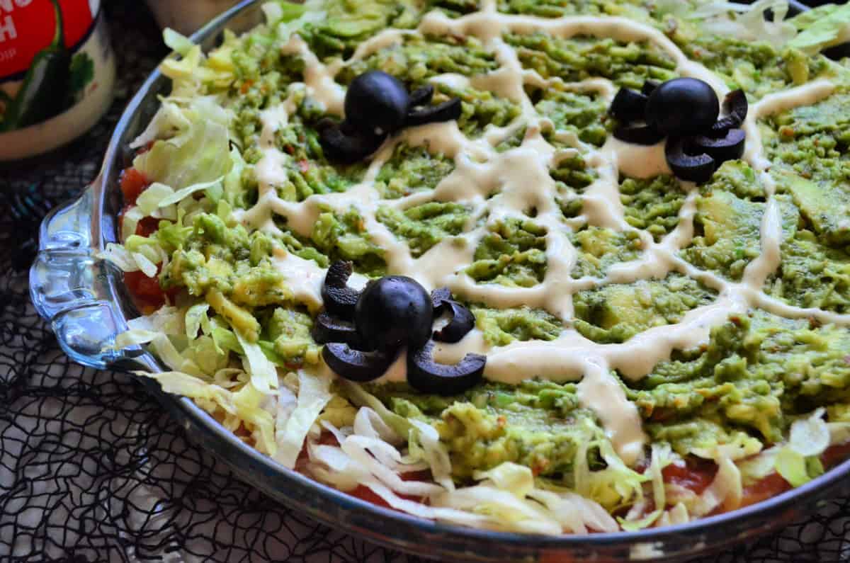 closeup view of 7 layer dip with ranch to look like web and olives cut into spiders.