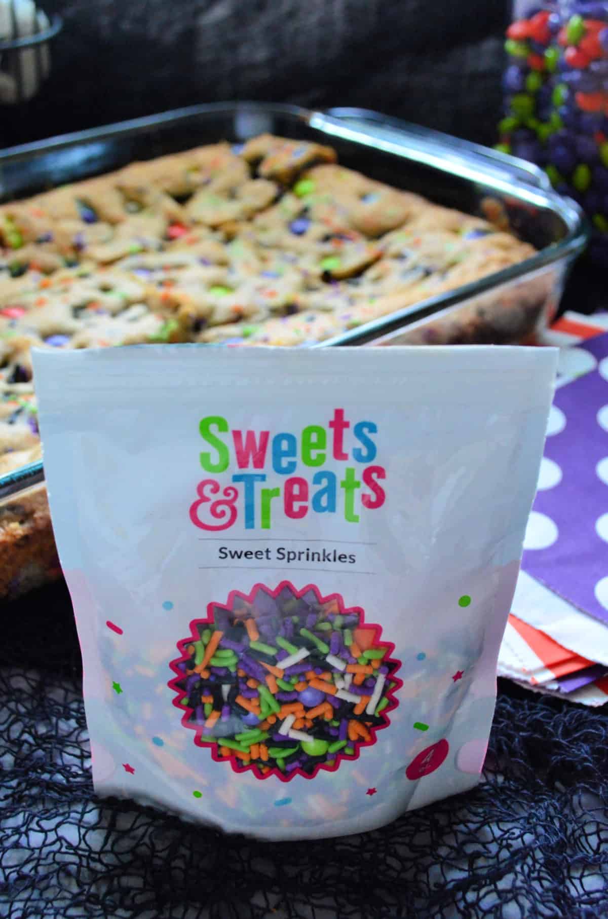 Bag of Sweets & Treats Sprinkles in orange, green, and purple with cookie bar in background.