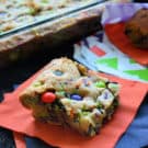 thick square cookie with orange, purple, and green m&ms inside on orange napkin.