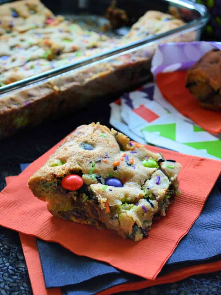 thick square cookie with orange, purple, and green m&ms inside on orange napkin.