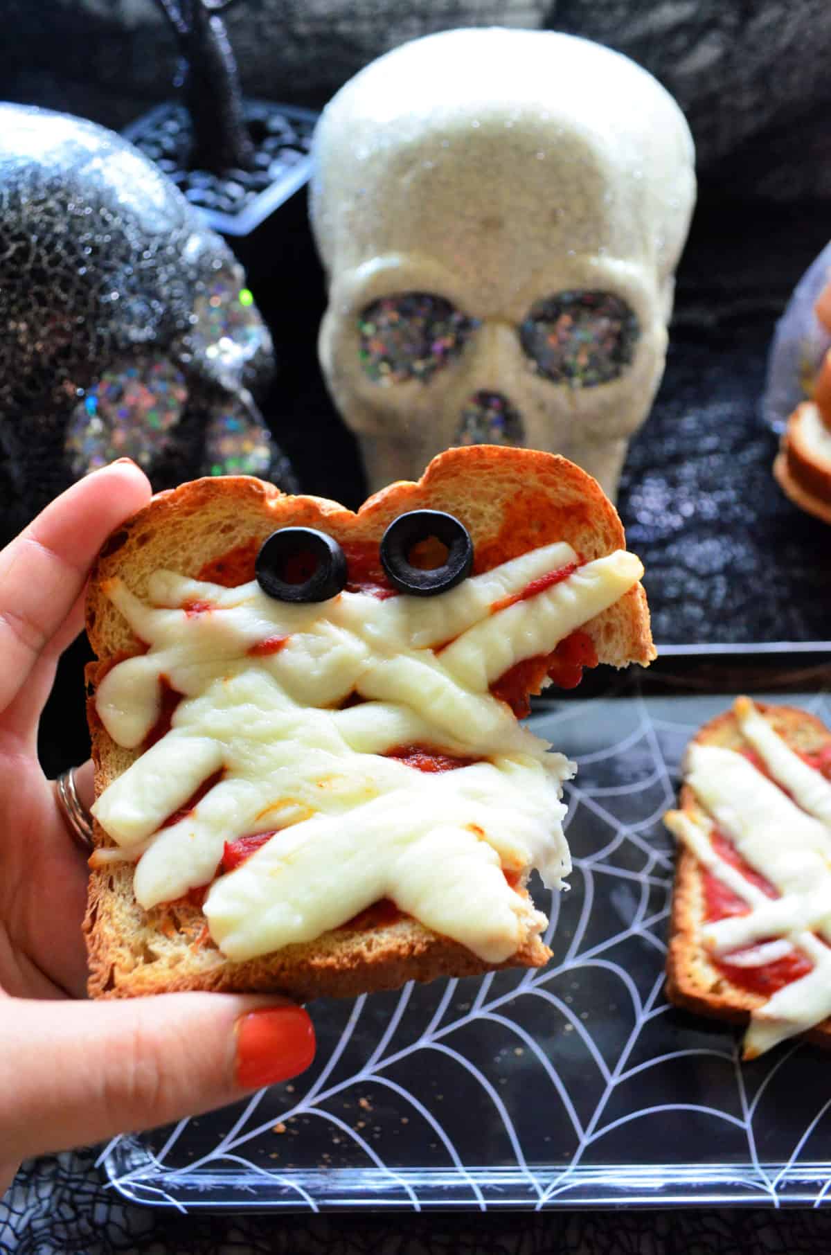 toast slice with marinara, mozzarella and olives to look like mummy face missing a bite.