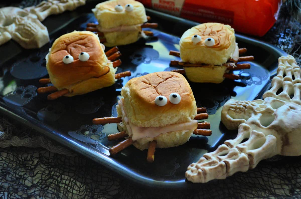 closeup of small turkey sandwiches with pretzels sticking out like spider legs, candy eyes on top. 