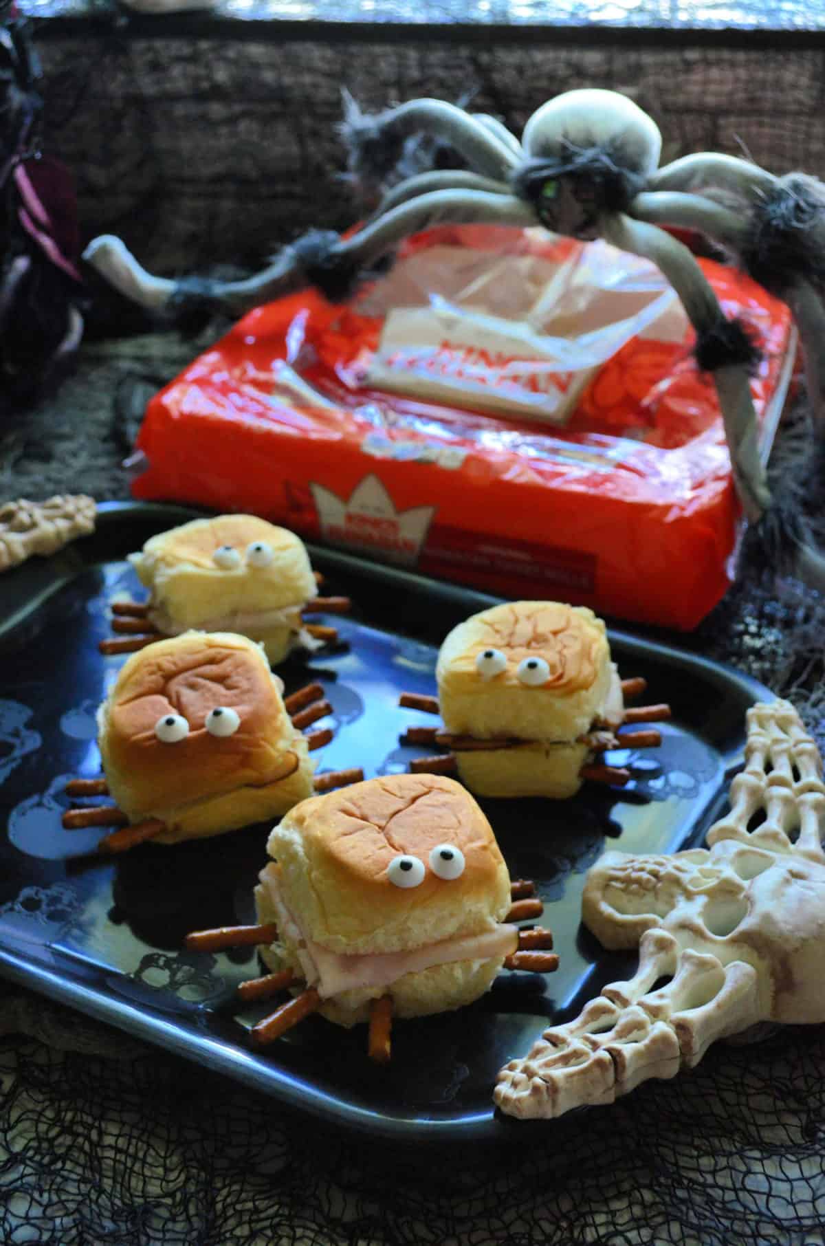 Plated mini spider sandwiches in front of King's Hawaiian rolls with fake spider on top of package.