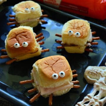 Close up of 4 Halloween Turkey & Cream Cheese Spider Sandwiches on black plate.