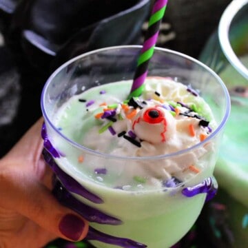 Close up of glass of creamy green drink topped with whipped cream, sprinkles, and candy monster eyeball.