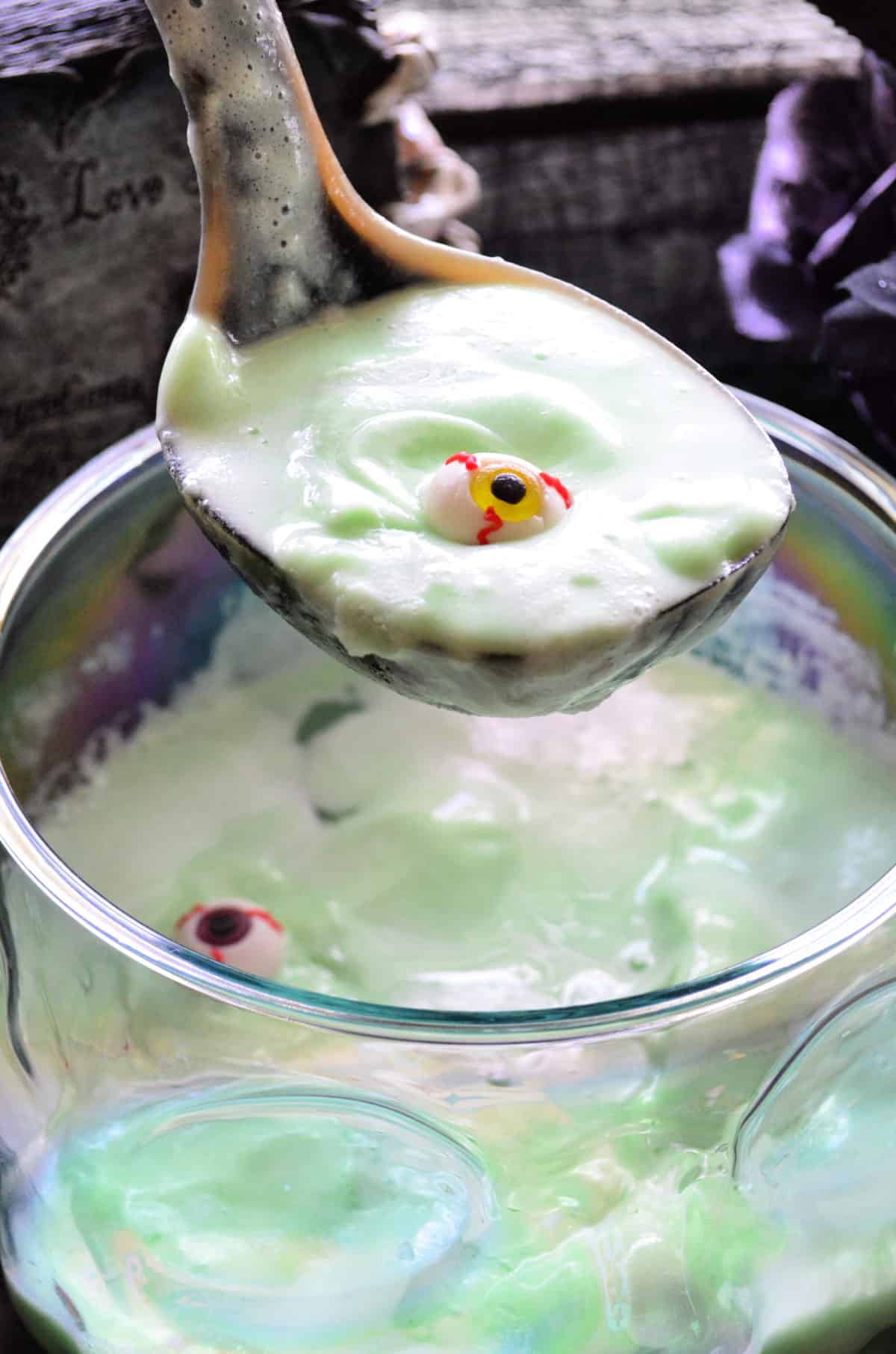 Ladle with creamy green liquid and candy eyeball over punch bowl of creamy green drink.