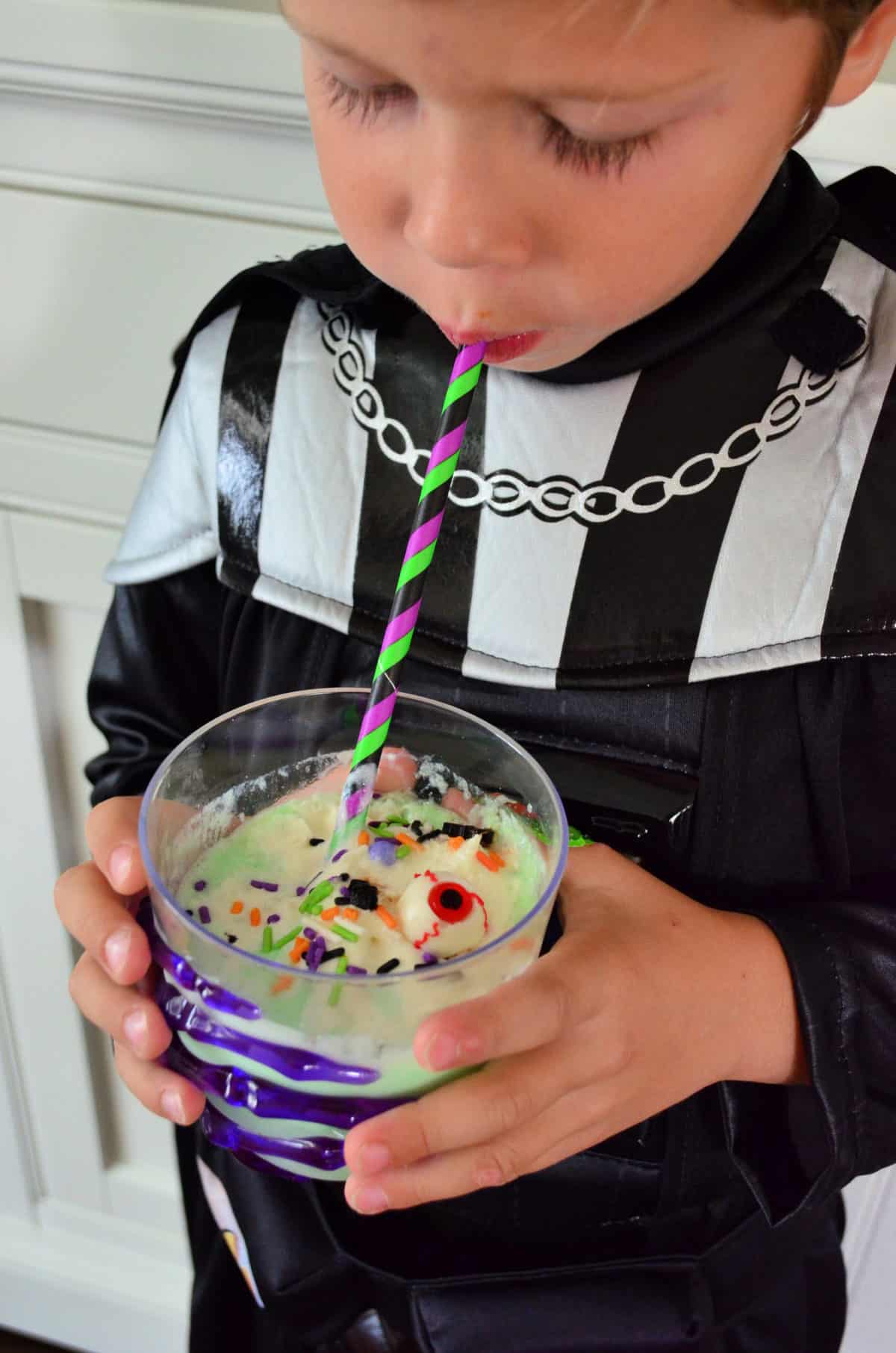 Costumed bow sipping green witch punch with candy eyeballs from paper straw.