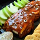 Closeup of sliced apples, crackers, and caramel cream cheese dip decorated with candy eyes.