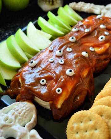 Closeup of sliced apples, crackers, and caramel cream cheese dip decorated with candy eyes.