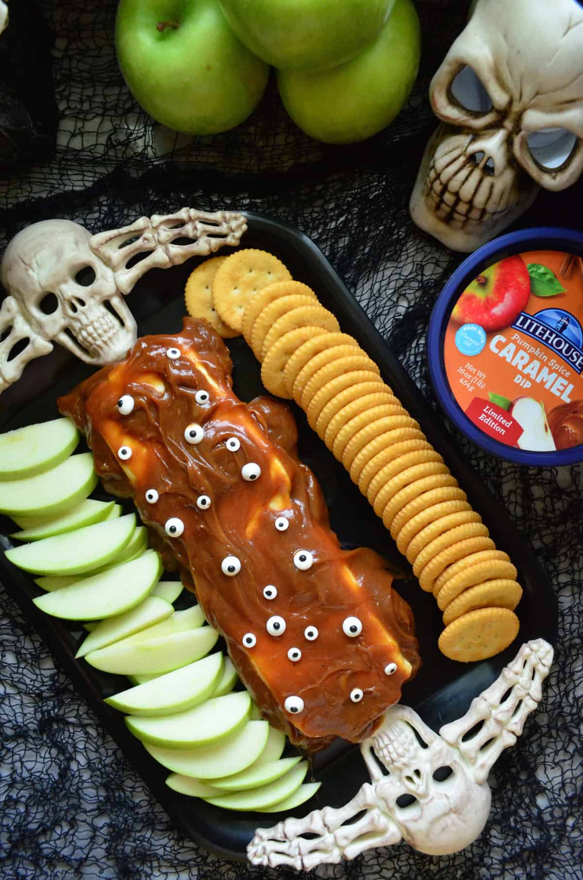 skull platter with cream cheese covered in caramel and candy eyes served with apples and crackers.