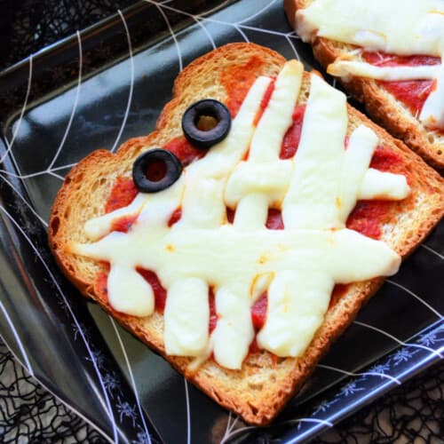 Black spider web tray with a slice of toast with tomato sauce and melted piece of cheese to look like a mummy with olive eye balls.