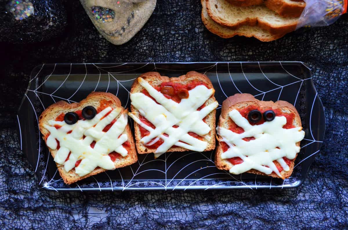 3 slices toast with marinara, mozzarella and olives to look like mummy faces on spiderweb platter.