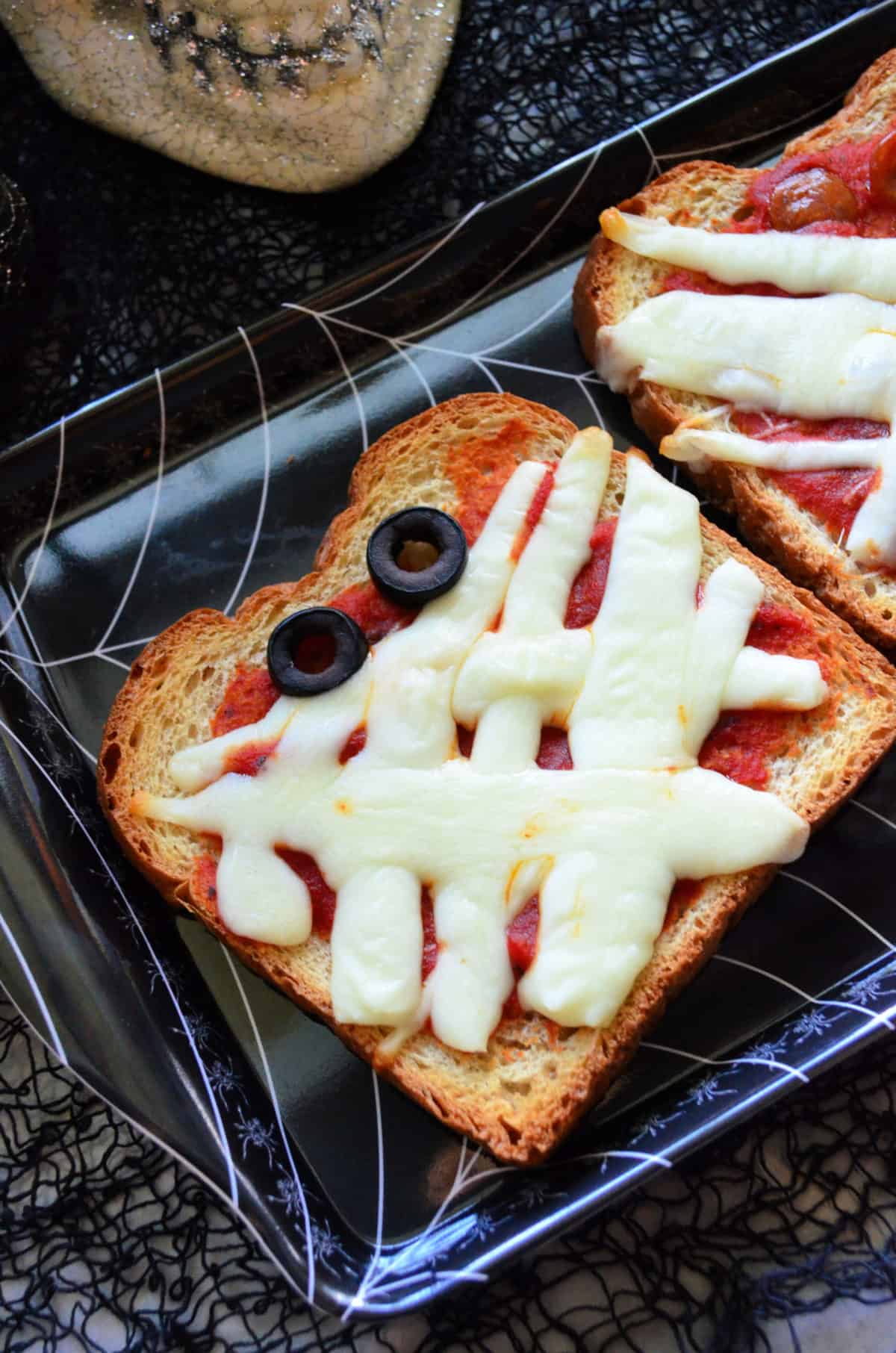 close-up of marinara, mozzarella, and black olives topping toast to look like mummy face.