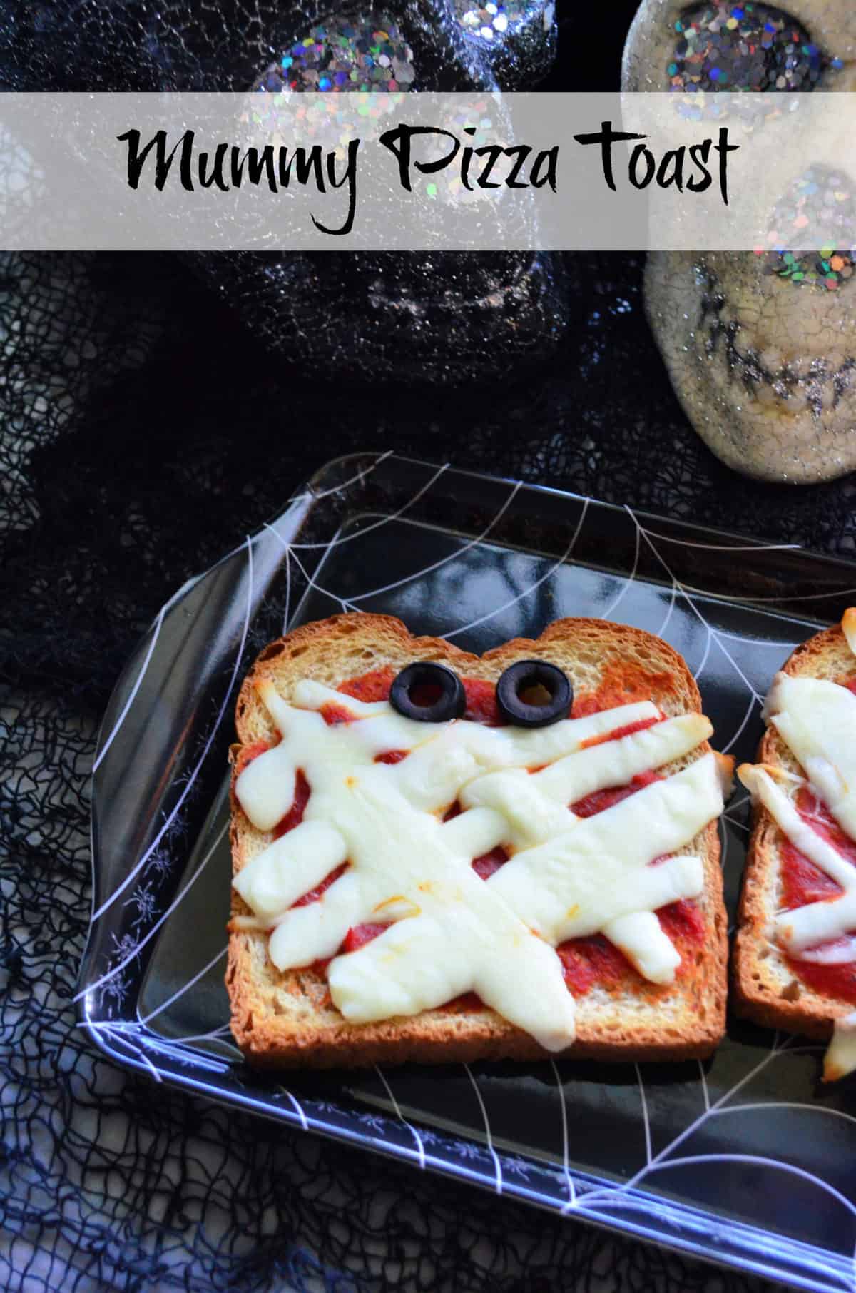 Toast with marinara, mozzarella and olives to look like mummy face on spiderweb platter with title text.