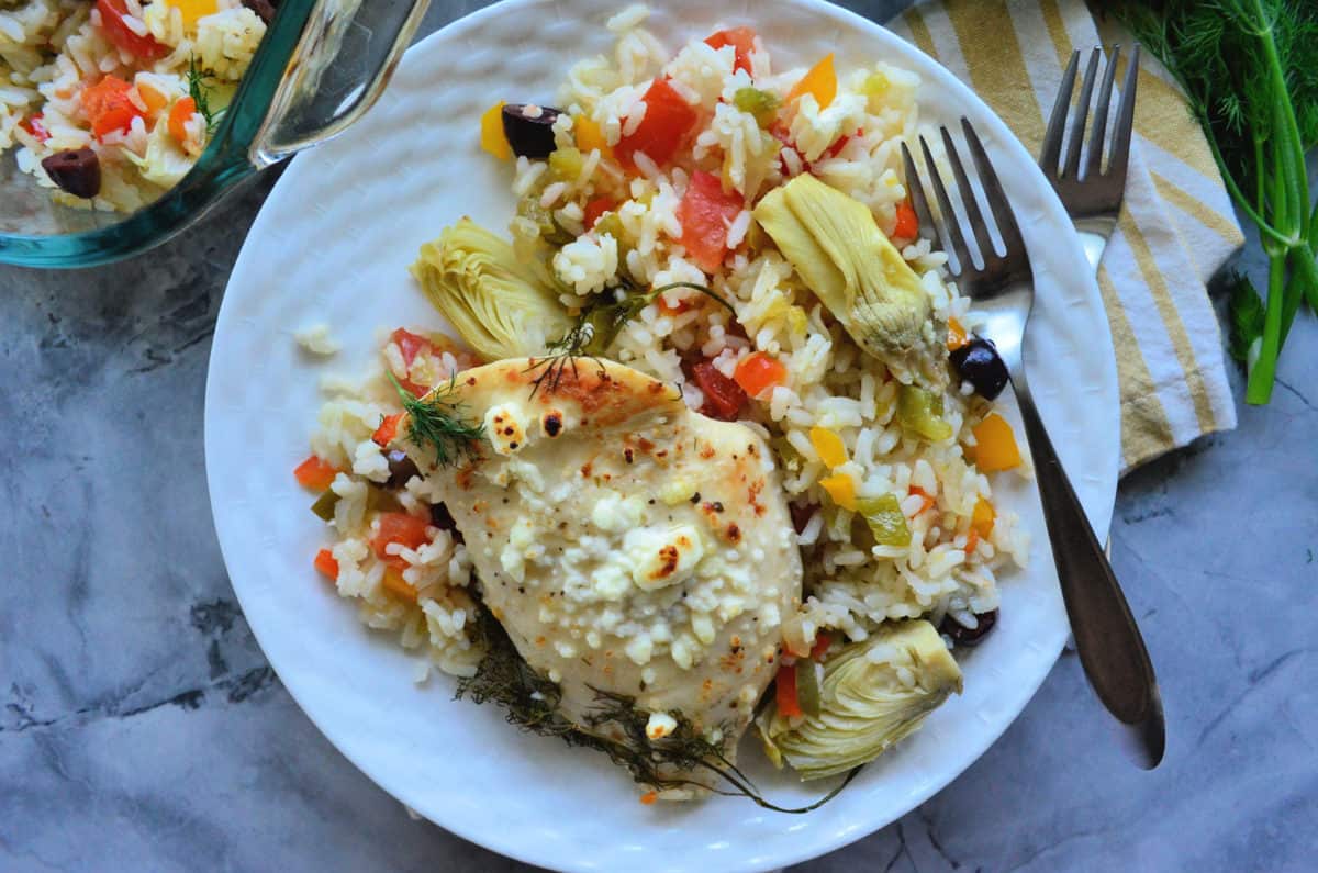 chicken over bed of rice with artichoke, bell pepper, kalamata, tomatoes, and dill with fork.