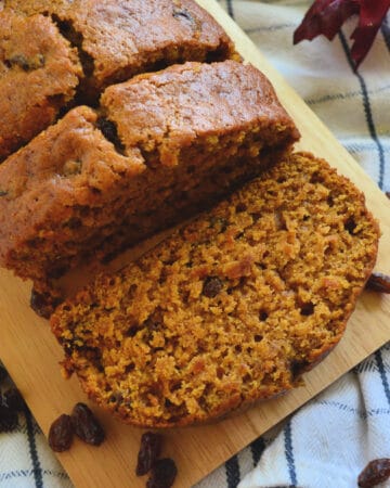 Top closeup view of pumpkin bread loaf on board with two slices cut and resting.