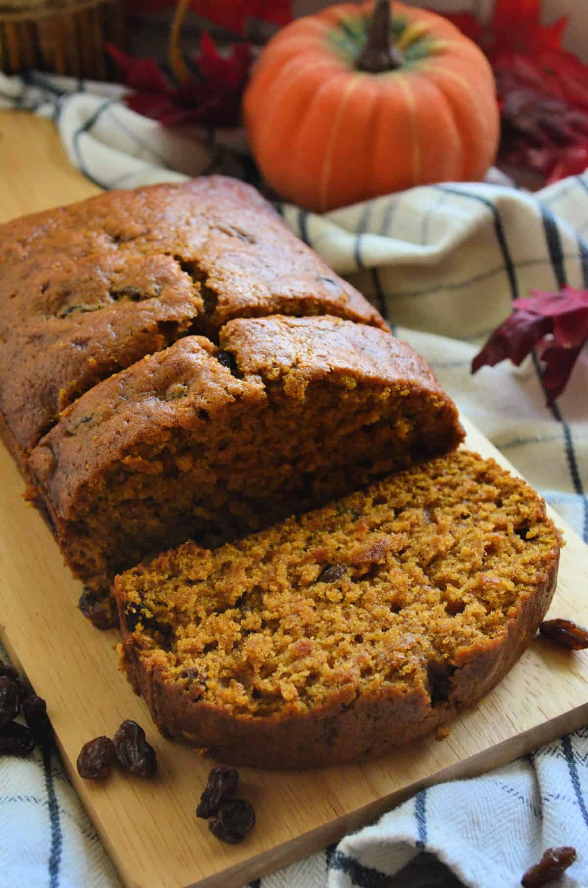 pumpkin bread with raisins on paddle with 2 pieces sliced in front of decorative pumpkin.