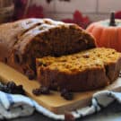 Pumpkin Bread with Raisins resting on board with one slice lying horizontal near mini pumpkin.