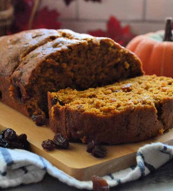 Pumpkin Bread with Raisins resting on board with one slice lying horizontal near mini pumpkin.