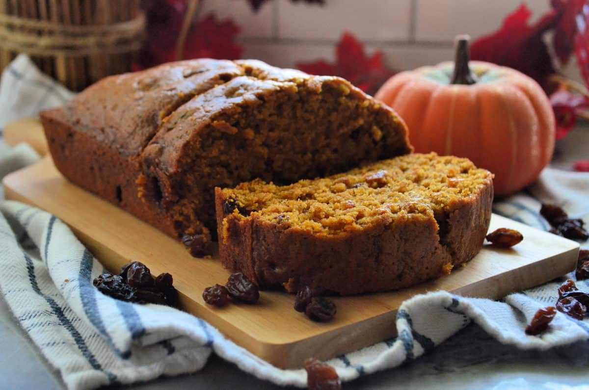 pumpkin bread with raisins on paddle with 2 pieces sliced in front of decorative pumpkin.