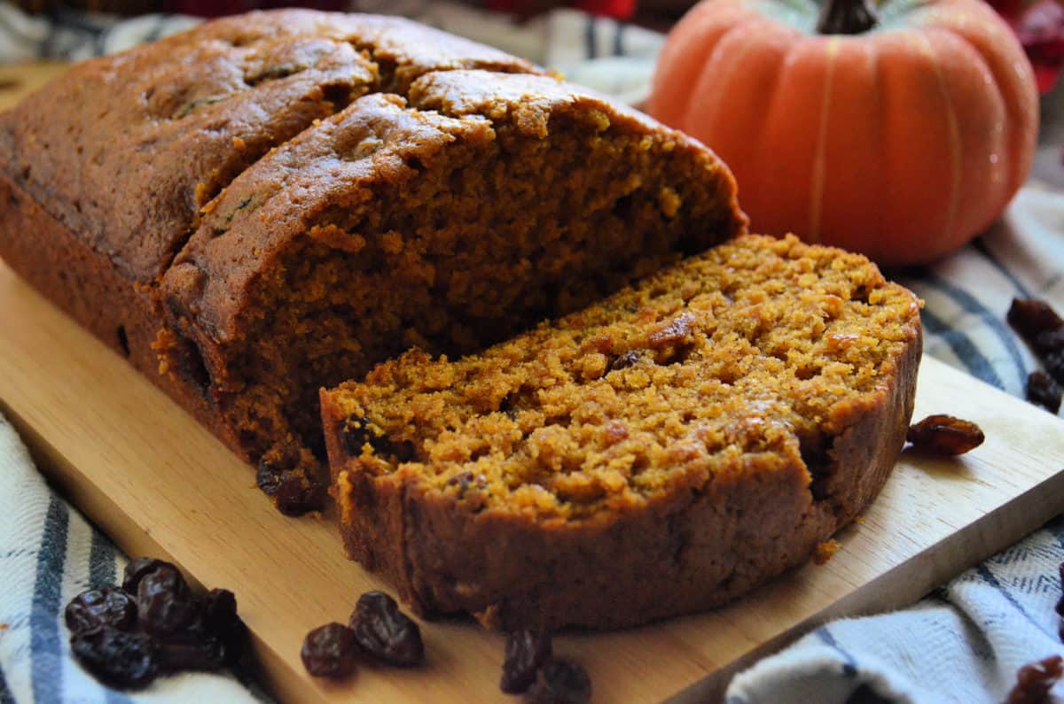 closeup pumpkin bread with raisins on paddle with 2 pieces sliced in front of decorative pumpkin.