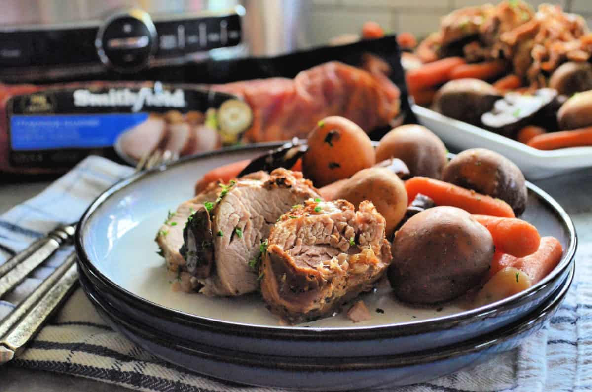 side view plated sliced tenderloin with potatoes, carrots, onions, and mushroom visible on placemat.